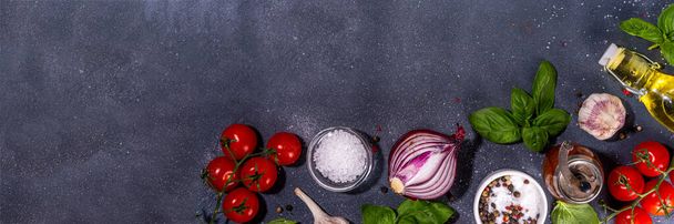Black cooking background with useful cooking italian Mediterranean ingredients - tomatoes, basil leaves, greens, olive oil, salt, pepper, garlic, flat lay black concrete table top view copy space  - 写真・画像