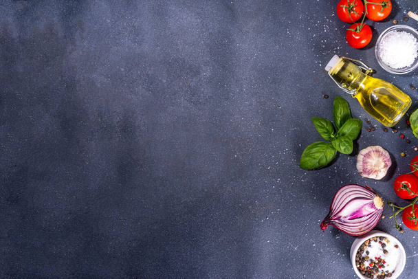 Black cooking background with useful cooking italian Mediterranean ingredients - tomatoes, basil leaves, greens, olive oil, salt, pepper, garlic, flat lay black concrete table top view copy space  - Photo, image
