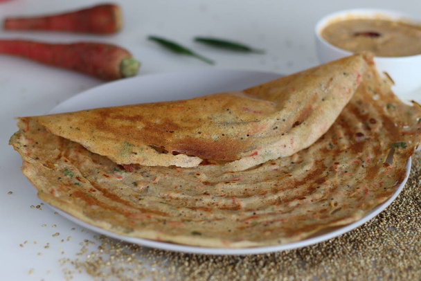 Carrot bajra ghee roast. Crispy crapes made of fermented batter of unpolished pearl millets and de husked black lentils with freshly grated carrots added into the batter. Served with coconut chutney - Photo, Image