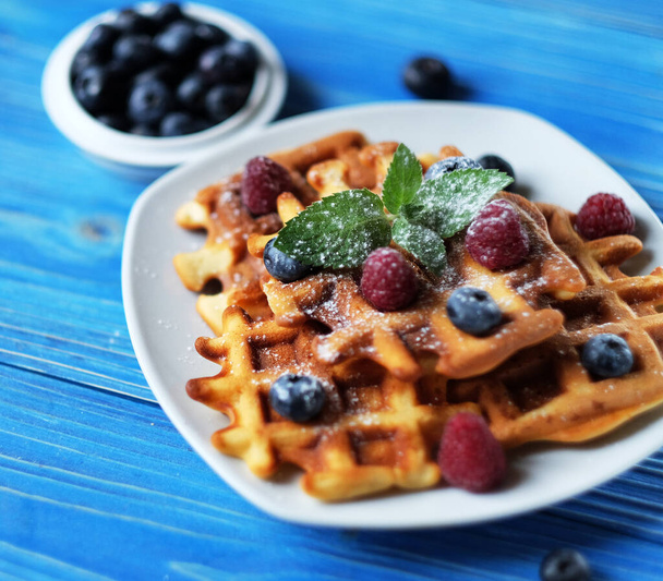 Waffles with blueberries and raspberries for breakfast over blue wooden table. Close up. - Valokuva, kuva