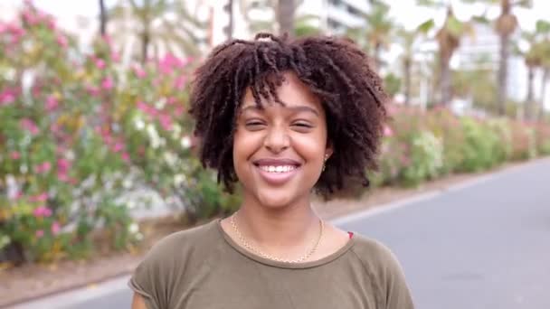 Portrait de joyeuse femme afro-américaine aux cheveux bouclés souriant à la caméra debout à l'extérieur. - Séquence, vidéo