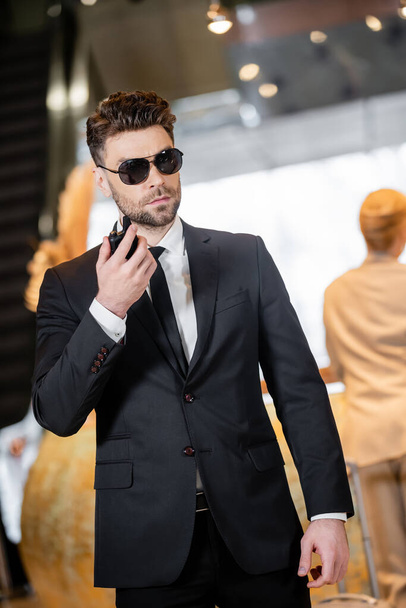 bodyguard concept, handsome man in formal wear and tie holding walkie talkie, private security, protecting female client on blurred background, connection and safety - Foto, Imagen