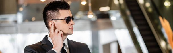 bodyguard concept, handsome man in formal wear and tie touching earpiece in lobby of hotel, security, communication, hotel safety, career in security, profession, banner  - Foto, imagen