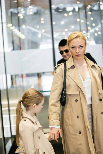 private security service, bodyguard in formal wear and sunglasses standing near hotel entrance, blonde woman and child entering hotel lobby, autumn fashion, warm clothing, luxury lifestyle  - Photo, Image