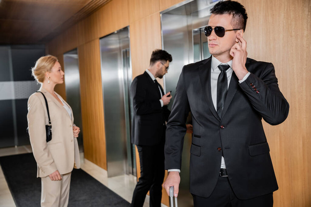 охоронна служба, особистий захист, блондинка в офіційному одязі стоїть біля ліфтів, співробітники охорони, що захищають успішну бізнес-леді в готелі, чоловіки в офіційному одязі  - Фото, зображення