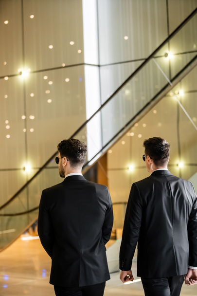 security management of luxury hotel, back view of two men in formal wear and sunglasses, bodyguards on duty, safety measures, vigilance, black suits, private security, strong guards  - Photo, Image