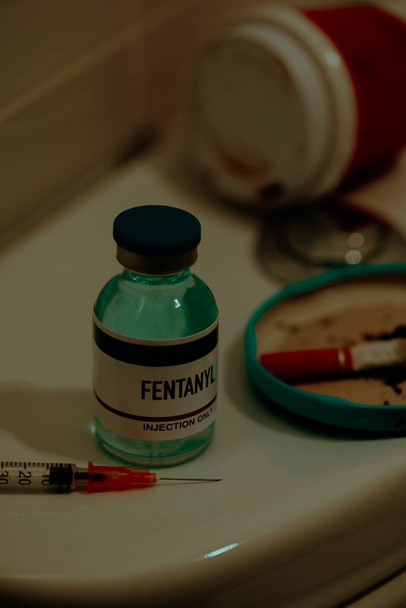 closeup of a syringe and a simulated vial of fentanyl on the cistern of a toilet next to a cigarette butt, in a restroom - Zdjęcie, obraz