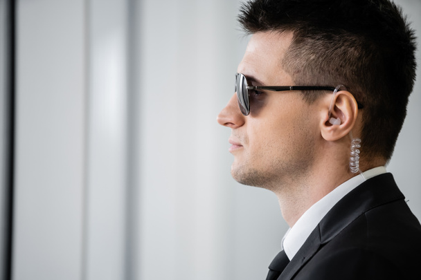 professional headshots, bodyguard work, side view of handsome man in sunglasses and black suit with tie, hotel safety, security management, surveillance and vigilance, guard on duty - Foto, imagen