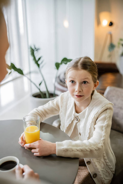 mother and daughter spending quality time together, preteen girl holding glass of orange juice and looking at mother, working parent and kid, modern parenting, family bonding, blurred foreground  - Photo, Image