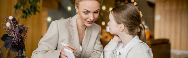 happy mother and daughter spending quality time together, blonde woman holding smartphone near daughter, digital age, working parent and kid, modern parenting, family bonding, banner  - Photo, Image