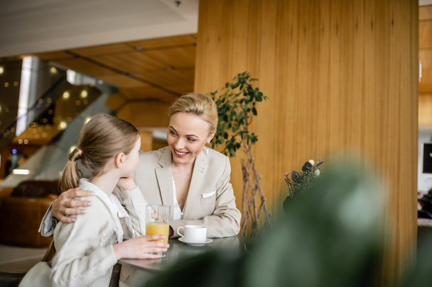 mother and daughter spending quality time together, blonde woman smiling and hugging preteen girl, orange juice and cup of coffee, working parent and kid, modern parenting, family bonding  - Photo, Image