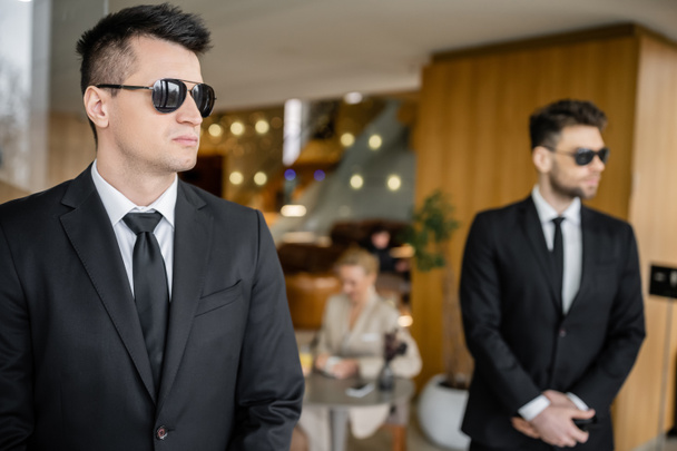 private security service, personal safety concept, handsome bodyguards in formal wear and sunglasses protecting safety of female client on blurred background, mother and daughter in cafe  - Photo, Image