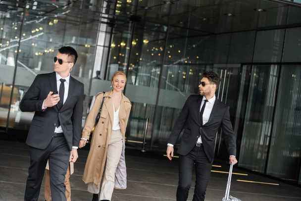 handsome bodyguards protecting privacy of female clients, happy woman and daughter walking out of hotel, personal safety of rich family, men in sunglasses and suit with luggage   - Photo, Image