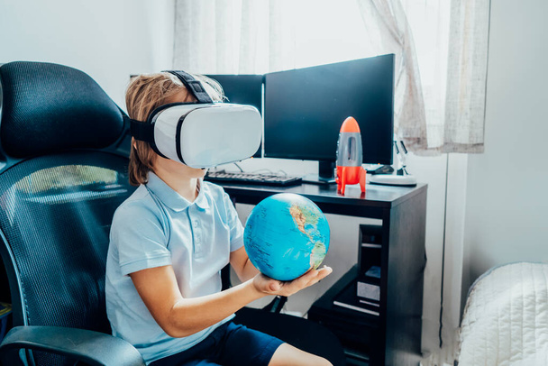 Boy studies space with help of technology and app. Kid in Virtual reality headset learning Solar system planets at home. Space explore with augmented reality glasses. Modern education science concept - Foto, Bild