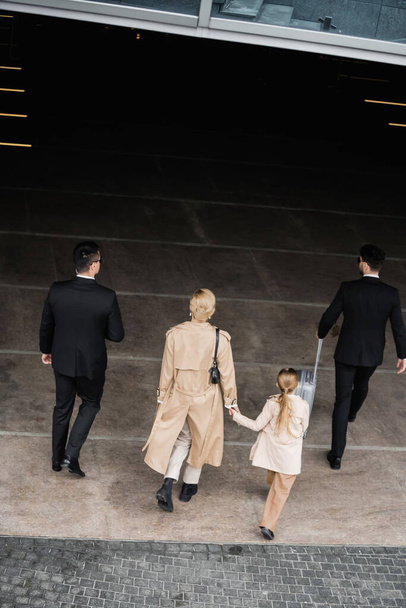 top view of bodyguards protecting privacy of female clients, blonde woman and daughter walking out of hotel, personal safety of rich family, men in formal wear and female clients   - Foto, immagini