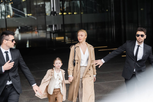 private security, personal bodyguards protecting female clients, blonde woman and daughter walking out of hotel, safety of rich family, men in formal wear and sunglasses on duty  - Foto, immagini