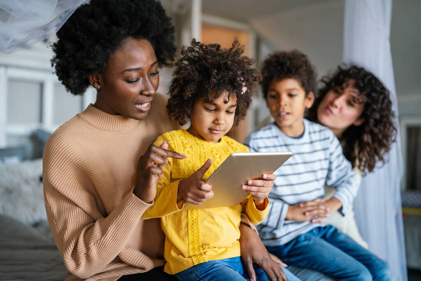 Счастливая многонациональная семья, весело проводящая время с цифровым устройством дома, домашние родители и маленькие дети, вместе пользующиеся цифровым планшетом. - Фото, изображение