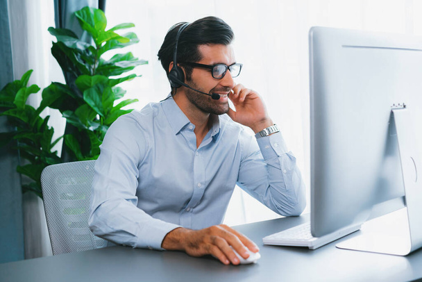 Male call center operator or telesales representative siting at his office desk wearing headset and engaged in conversation with client providing customer service support or making a sale. fervent - 写真・画像