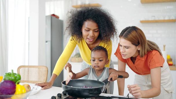 Boldog homoszexuális leszbikus pár és amerikai afrikai örökbefogadott gyermek élvezi főzés konyha szobában otthon. Leszbikus házasság és örökbefogadás. Homoszexuális család, LMBTQ életmód - Fotó, kép