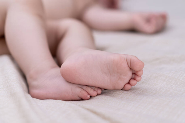 Barefoot little boy lying on white sheet laid on soft bed in nursery in early morning bare tender feet of baby relaxing at home after waking up closeup - 写真・画像