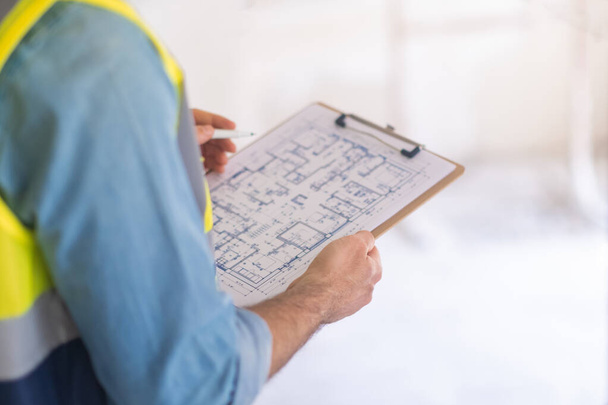 Professional architect holding clipboard with apartment drawing paper in hands man in uniform examining project plan getting ready for renovation process - Photo, Image