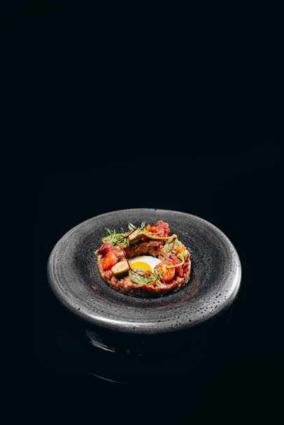 A cold appetizer of beef tartar with egg and stewed tomatoes - 写真・画像