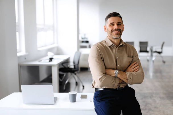 Successful businessman. Confident man in shirt sitting on desk, posing with folded arms, looking and smiling at camera, copy space, place for advertisement - Photo, Image