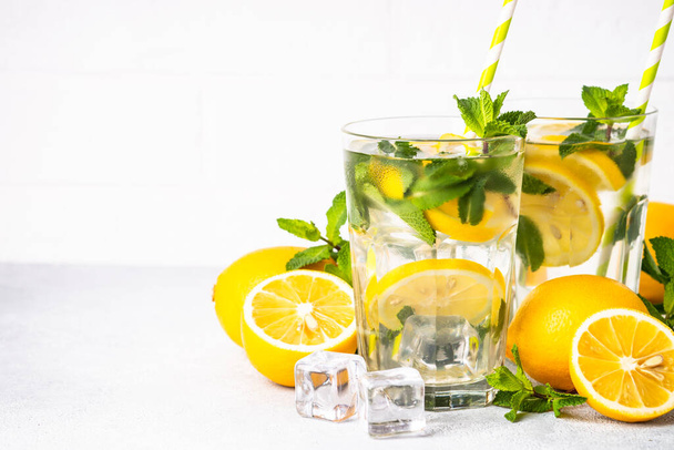 Lemonade in glass on white table with fresh lemons and mint. Cold summer drink. - Foto, afbeelding