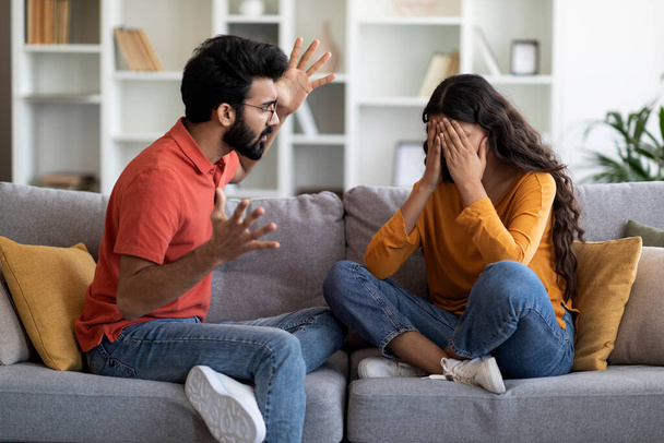 二つの対立。夫と議論しながら自宅で泣く若い女性を動揺,関係危機に苦しんでいる若いインドの家族,リビングルームで妻と感情的に話す怒っている男 - 写真・画像