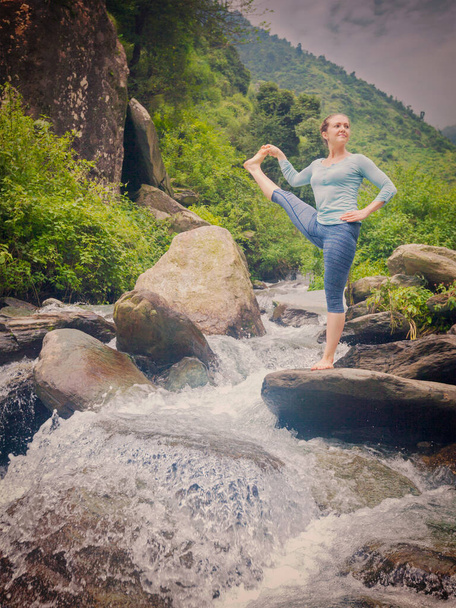 Йога на відкритому повітрі - жінка, що робить Ashtanga Vinyasa Yoga balance asana Utthita Padangushthasana - розширена позиція ручної пози на відкритому повітрі у водоспаді. Урожай ретро ефект фільтрованого зображення - Фото, зображення