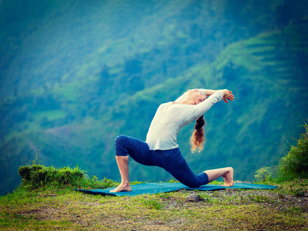 Йога под открытым небом - спортивная фитнес-женщина практикует хатха-йогу асана - низкую позу полумесяца на открытом воздухе в горах Алая. Винтажный ретро-эффект фильтрует образ хипстера
. - Фото, изображение