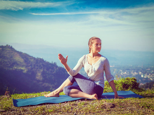 Yoga oefening buiten - vrouw doet Ardha matsyendrasana asana - halve wervelkolom draai pose bergen in Himalaya in India in de ochtend. Vintage retro effect gefilterd hipster stijl afbeelding. - Foto, afbeelding