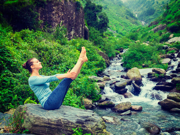 Yoga buiten - vrouw doet Ashtanga Vinyasa Yoga asana Navasana - boot pose - in Himalaya bij tropische waterval. Himachal Pradesh, India. Vintage retro effect gefilterd hipster stijl afbeelding - Foto, afbeelding