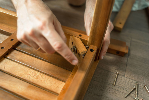 Ein Mann stellt einen Holztisch her. Ein Meister mit Werkzeug repariert Möbel. Reparatur des Stuhls. Papa sammelt Möbel zu Hause. Restaurierung von Wohnmöbeln - Foto, Bild