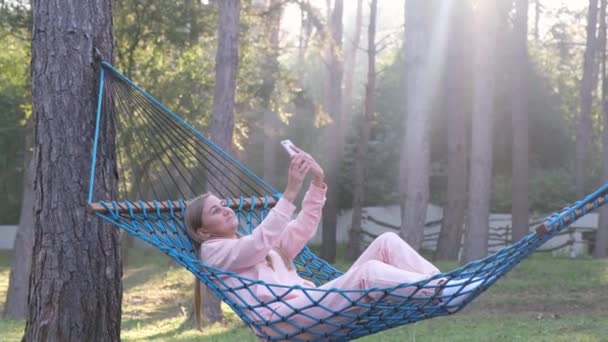 Woman with phone resting lying on hammock with mobile phone, take selfie, chat. - Video