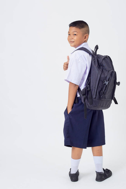 Un joven asiático lindo niño de pie en un uniforme escolar tailandés con una bolsa de mochila y libro sobre una pancarta de fondo blanco. Regreso a la escuela - Foto, imagen