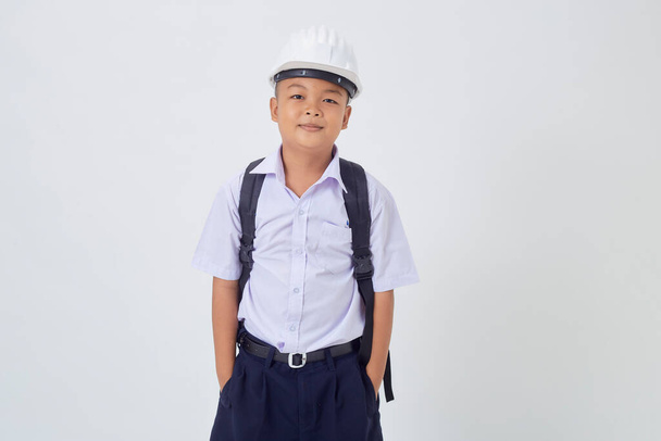 A young Asian cute boy standing in a Thai school uniform with a backpack bag and safety helmet  on a white background banner. Back to school - Photo, Image