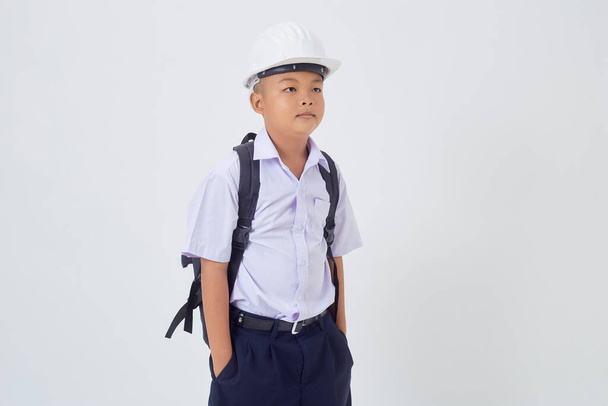 Um menino bonito asiático jovem de pé em um uniforme escolar tailandês com uma mochila e capacete de segurança em um banner de fundo branco. De volta à escola - Foto, Imagem