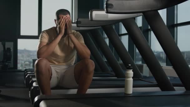 Épuisé afro-américain latino sportif repos après avoir couru sur tapis roulant entraînement cardio dans la salle de gym fatigué homme coureur homme sport entraîneur boire de l'eau potable de la bouteille de sport rafraîchir la soif du corps - Séquence, vidéo