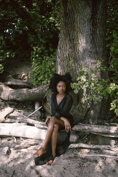 Fashion outdoor beach portrait Beautiful young African American Black woman posing outside on sandy coast with big green trees on sunny summer day. Cosmetology, natural skin body care and spa - 写真・画像