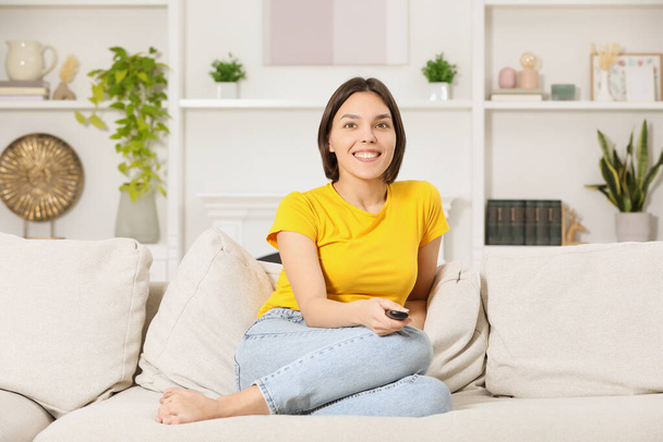 Happy woman watching TV on sofa at home - Foto, afbeelding