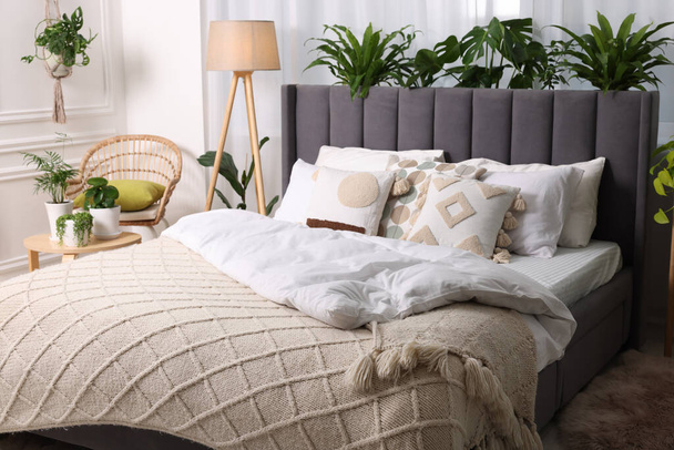 Comfortable bed, wicker armchair, lamp and beautiful houseplants in room. Bedroom interior - Fotografie, Obrázek
