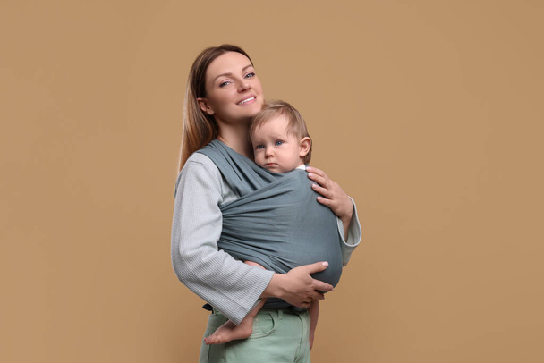 Mother holding her child in baby wrap on light brown background - Valokuva, kuva