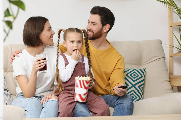 Happy family watching TV with popcorn on sofa indoors, space for text - Foto, imagen