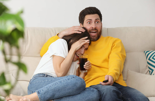 Frightened couple watching TV on sofa at home - Photo, Image
