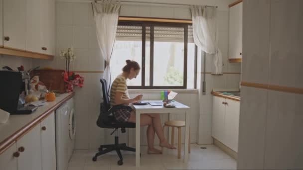 Uma mulher adulta tomando um café da manhã na mesa da cozinha olhando para seu laptop. A meio do tiro - Filmagem, Vídeo