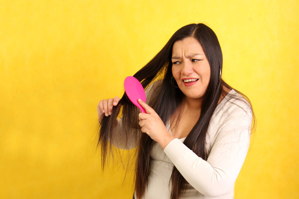Aikuinen 40-vuotias latinonainen harjaa hiuksensa vaikeuksitta, koska se on hyvin sotkeutunut kuivumisen aiheuttamien solmujen vuoksi. - Valokuva, kuva