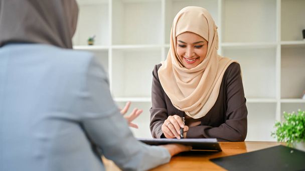 A beautiful Asian Muslim businesswoman is in the meeting with her financial consultant, looking at a tablet screen while talking and planning an investment plan together. - Foto, Bild