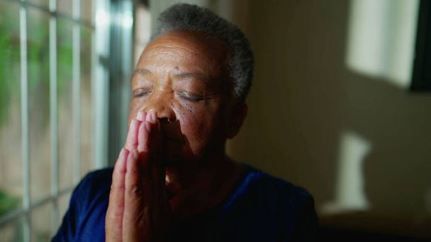 Одна літня чорношкіра жінка Молиться вікном, побожна афроамериканська старша в молитві та медитації в приміщенні, поклоніння і HOPE - Фото, зображення