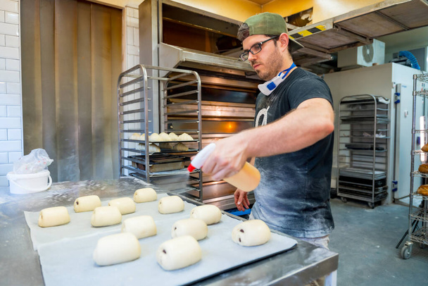 Boulanger de boulangerie dans l'atelier de boulangerie artisanale préparant croissant et napolitain sur les plateaux - Photo, image